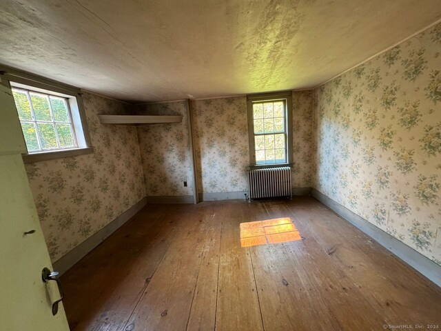 spare room featuring a textured ceiling, radiator, vaulted ceiling, and hardwood / wood-style flooring