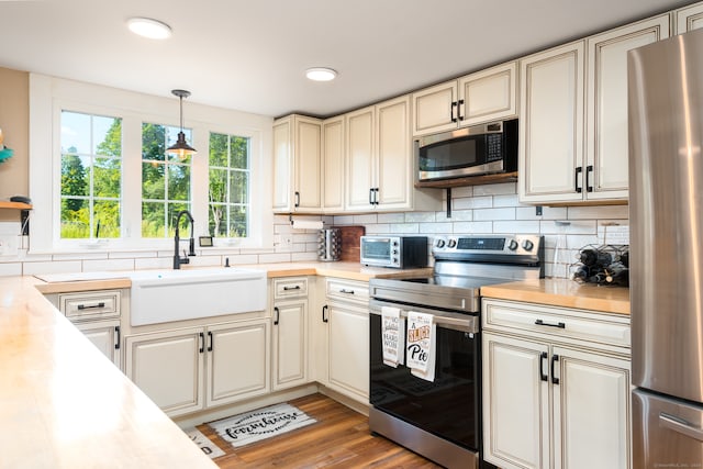 kitchen with tasteful backsplash, appliances with stainless steel finishes, light wood-type flooring, pendant lighting, and sink