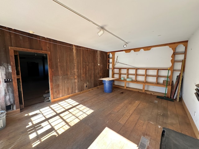 interior space with rail lighting, wood-type flooring, and wooden walls