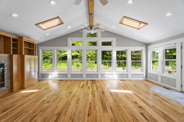 interior space featuring a tile fireplace, ceiling fan, vaulted ceiling with skylight, and light wood-type flooring