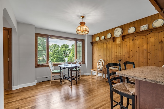 dining area with light hardwood / wood-style floors, wooden walls, baseboard heating, and a notable chandelier