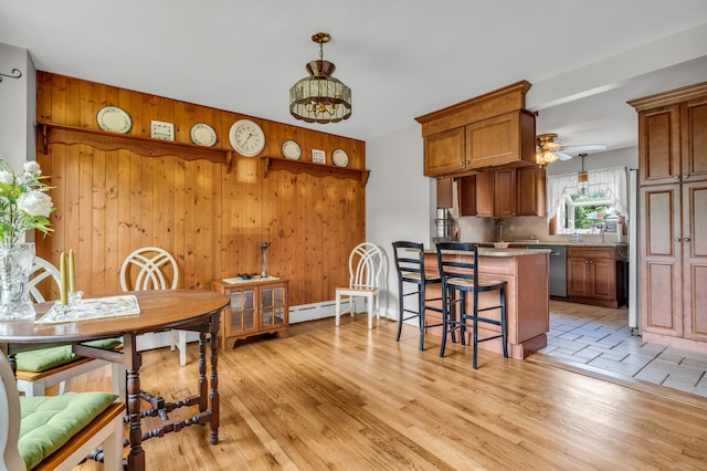 interior space with kitchen peninsula, ceiling fan, light hardwood / wood-style flooring, decorative light fixtures, and wooden walls