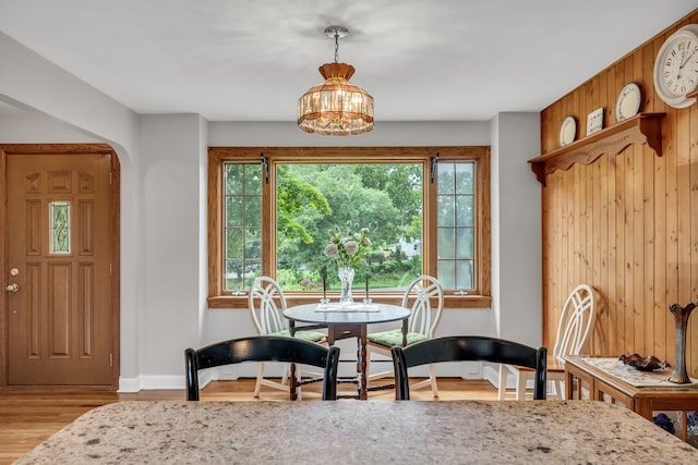 dining area with a chandelier, light hardwood / wood-style floors, and wood walls