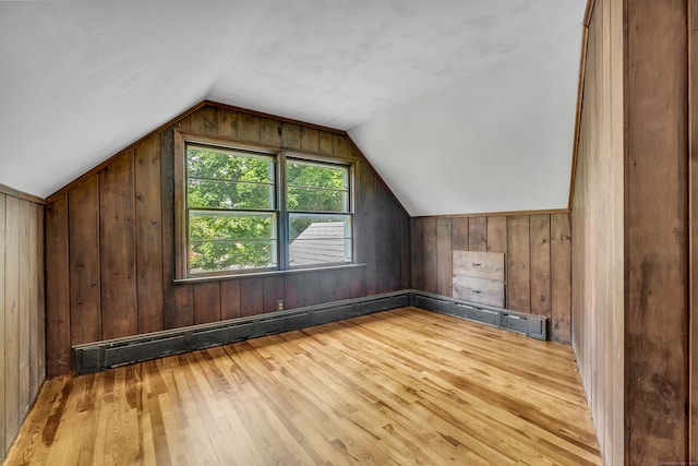 additional living space with light wood-type flooring, lofted ceiling, wood walls, and a baseboard heating unit