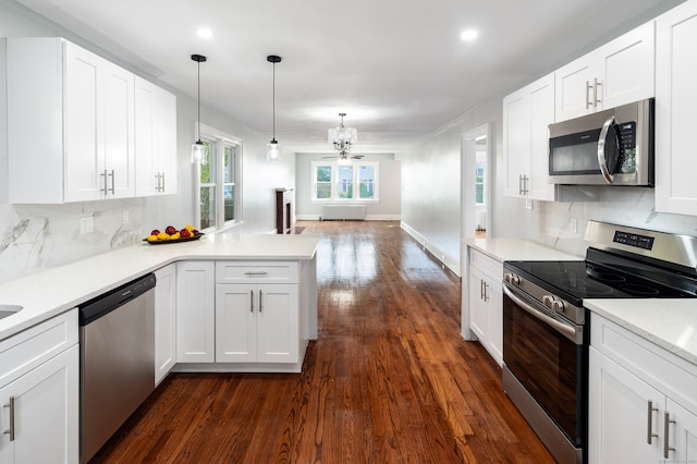 kitchen featuring kitchen peninsula, stainless steel appliances, dark wood-type flooring, pendant lighting, and white cabinetry