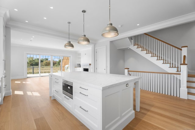 kitchen with pendant lighting, light stone counters, white cabinets, a kitchen island, and light hardwood / wood-style flooring