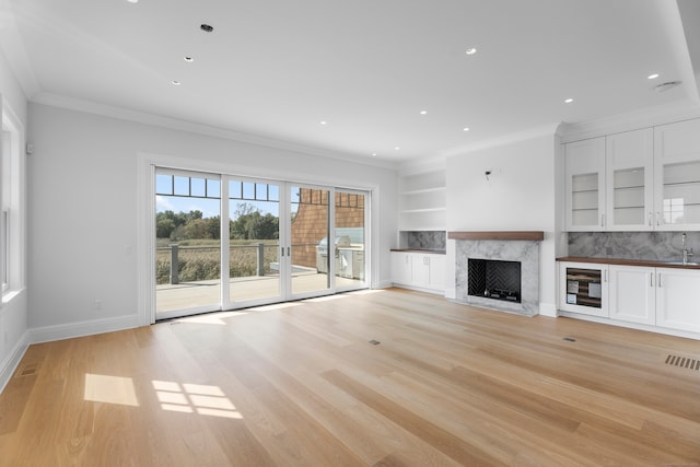 unfurnished living room with light hardwood / wood-style floors, a high end fireplace, beverage cooler, built in features, and ornamental molding