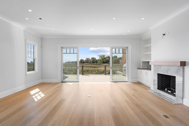 unfurnished living room with built in shelves, a fireplace, ornamental molding, and light hardwood / wood-style flooring