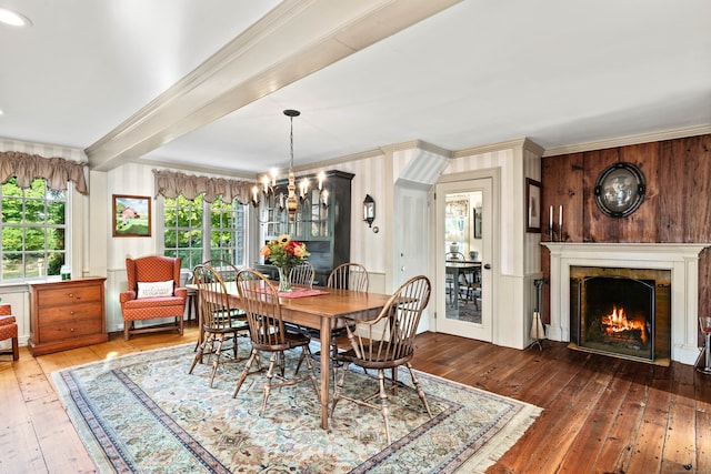 dining area with dark wood-type flooring, wood walls, beamed ceiling, an inviting chandelier, and ornamental molding