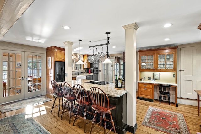 kitchen featuring light wood-type flooring, french doors, decorative columns, a breakfast bar, and light stone countertops