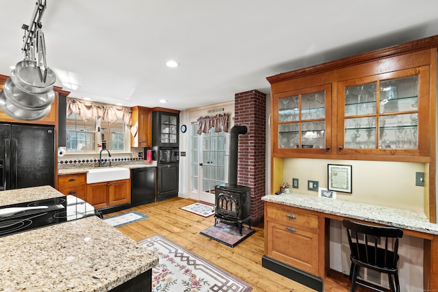 kitchen featuring sink, a wood stove, light hardwood / wood-style flooring, decorative backsplash, and black appliances