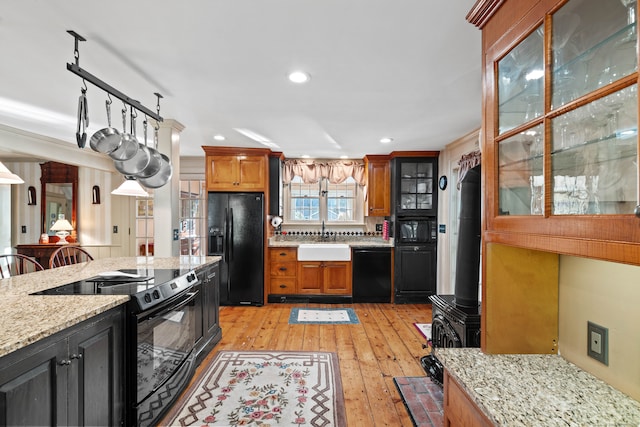 kitchen featuring decorative backsplash, light hardwood / wood-style floors, light stone countertops, black appliances, and sink