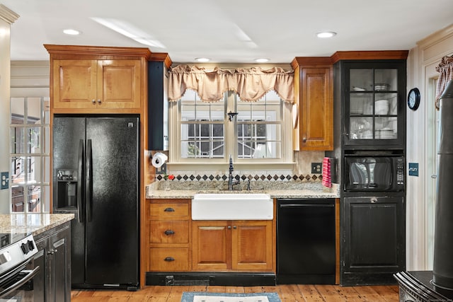 kitchen featuring light stone countertops, light wood-type flooring, black appliances, and sink