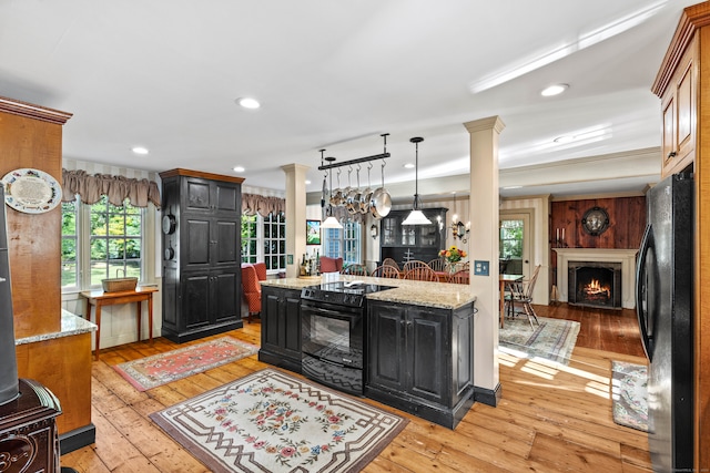 kitchen featuring decorative columns, black appliances, light hardwood / wood-style floors, and hanging light fixtures