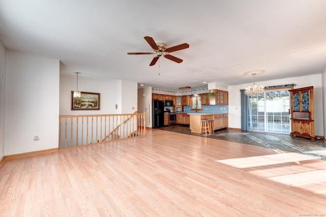 unfurnished living room featuring light hardwood / wood-style flooring and ceiling fan with notable chandelier