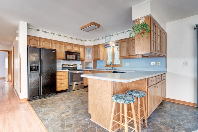 kitchen featuring black appliances, sink, kitchen peninsula, hardwood / wood-style floors, and a breakfast bar area