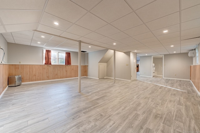 basement featuring a drop ceiling, light wood-type flooring, and wooden walls