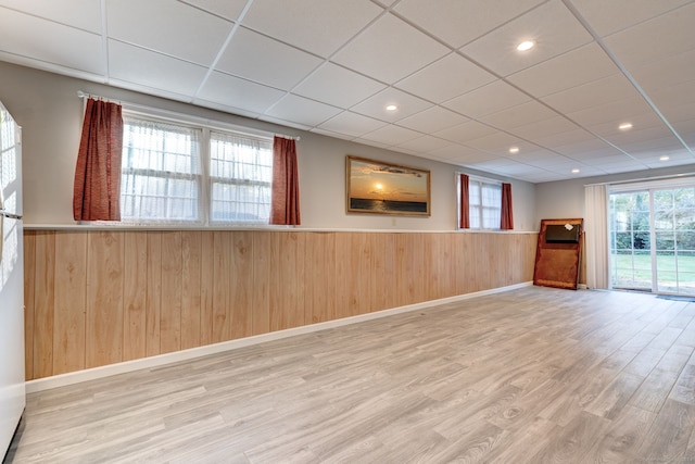 basement with wood walls, wood-type flooring, a wealth of natural light, and a drop ceiling