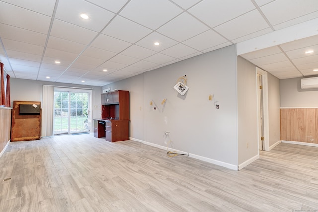 unfurnished living room with an AC wall unit, a paneled ceiling, and light wood-type flooring