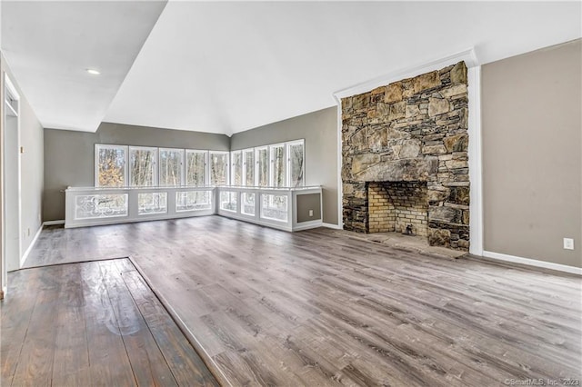 unfurnished living room featuring a stone fireplace, vaulted ceiling, and hardwood / wood-style floors