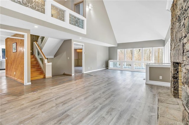 unfurnished living room with hardwood / wood-style flooring, a stone fireplace, and high vaulted ceiling