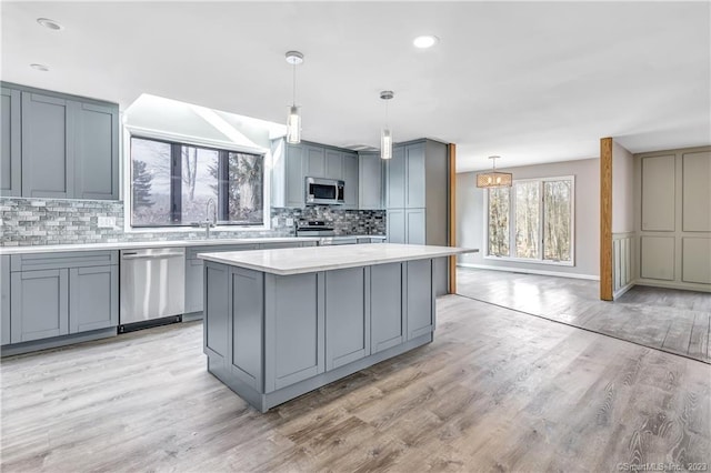 kitchen with pendant lighting, gray cabinetry, appliances with stainless steel finishes, a center island, and light hardwood / wood-style floors