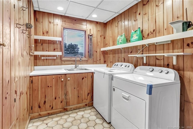 laundry room with cabinets, wooden walls, washer and clothes dryer, and sink