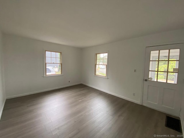 unfurnished room featuring a healthy amount of sunlight, baseboards, visible vents, and dark wood-style flooring