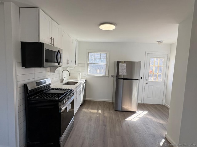 kitchen with stainless steel appliances, decorative backsplash, white cabinetry, a sink, and light wood-type flooring