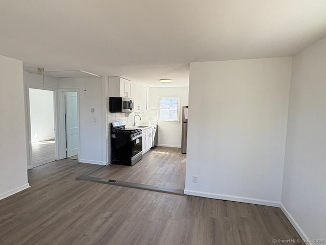 kitchen featuring stainless steel appliances, dark wood-type flooring, a sink, white cabinetry, and baseboards