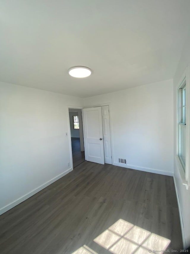 unfurnished room featuring visible vents, baseboards, and dark wood finished floors