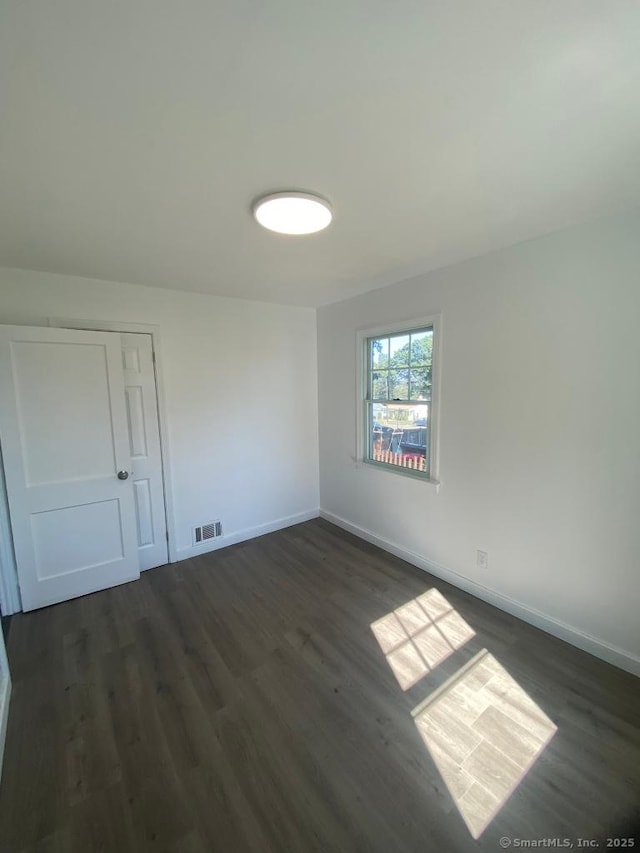 unfurnished room featuring dark wood-style floors, baseboards, and visible vents