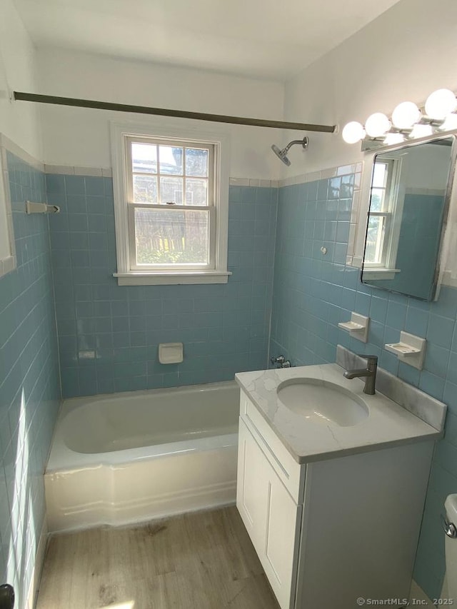 bathroom featuring a wealth of natural light, bathing tub / shower combination, wood finished floors, and tile walls