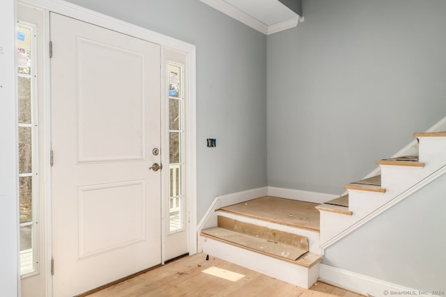 foyer featuring light wood-type flooring, ornamental molding, and a healthy amount of sunlight