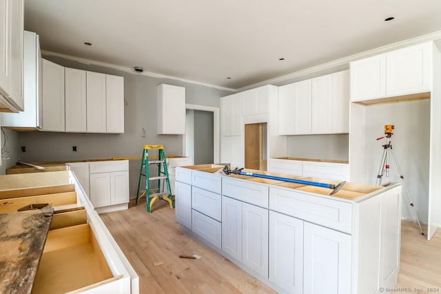 kitchen with light wood-type flooring, crown molding, and white cabinetry