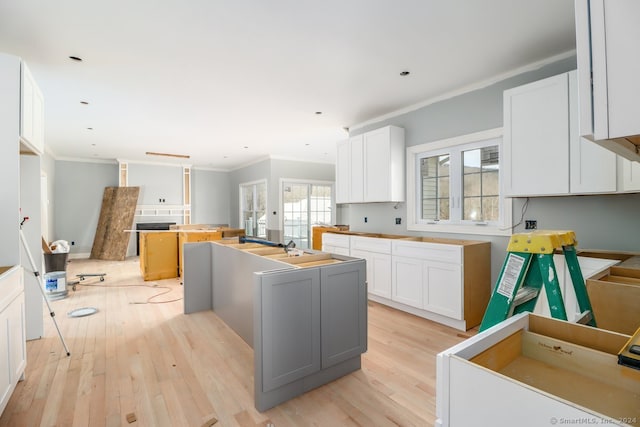 kitchen featuring white cabinets, french doors, a center island with sink, light hardwood / wood-style flooring, and crown molding