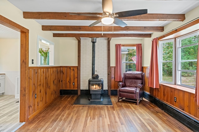 living area featuring light wood-type flooring, beam ceiling, and a wood stove