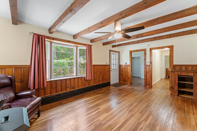 living room with light hardwood / wood-style floors, wood walls, baseboard heating, beamed ceiling, and ceiling fan