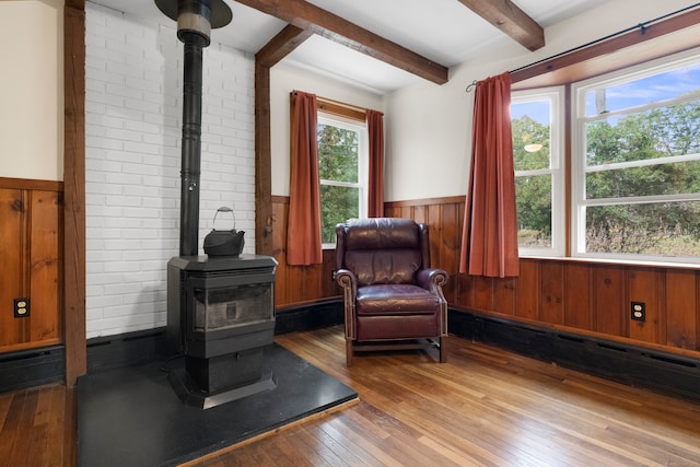 living area with light hardwood / wood-style floors, wood walls, beamed ceiling, a wood stove, and a baseboard heating unit