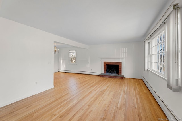 unfurnished living room featuring a brick fireplace, a baseboard heating unit, a notable chandelier, and light wood-type flooring