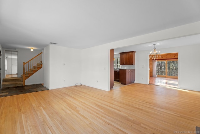 unfurnished living room with an inviting chandelier and light hardwood / wood-style floors