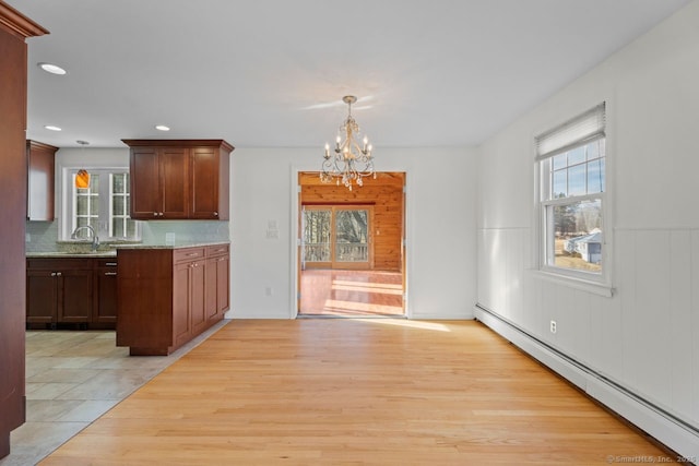 kitchen with pendant lighting, sink, a baseboard heating unit, a notable chandelier, and light stone counters