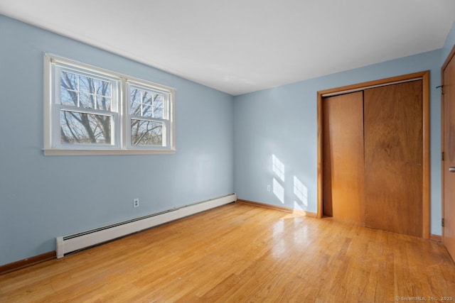 unfurnished bedroom featuring a baseboard heating unit, light hardwood / wood-style flooring, and a closet