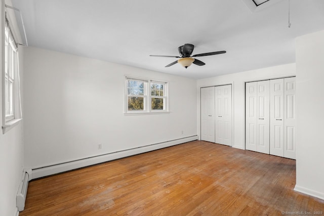 unfurnished bedroom with ceiling fan, a baseboard radiator, multiple closets, and hardwood / wood-style flooring