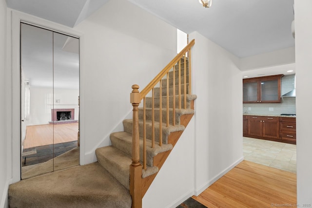 stairs with wood-type flooring and a brick fireplace