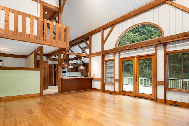 unfurnished living room featuring light wood-type flooring, a healthy amount of sunlight, beam ceiling, and high vaulted ceiling