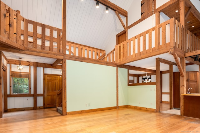 unfurnished living room with beam ceiling, light hardwood / wood-style flooring, a chandelier, high vaulted ceiling, and wooden ceiling