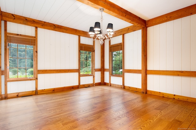 spare room with hardwood / wood-style flooring, wooden walls, a notable chandelier, and a wealth of natural light