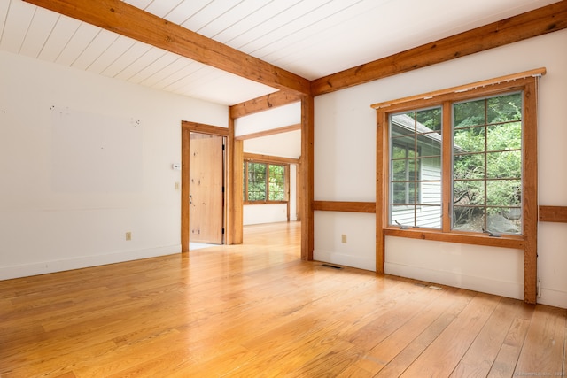 empty room with beam ceiling, light hardwood / wood-style floors, and a wealth of natural light