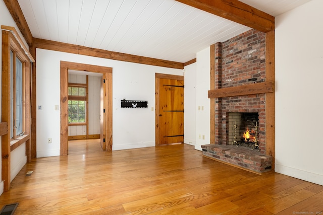 unfurnished living room featuring a brick fireplace, light wood-type flooring, beamed ceiling, and wood ceiling